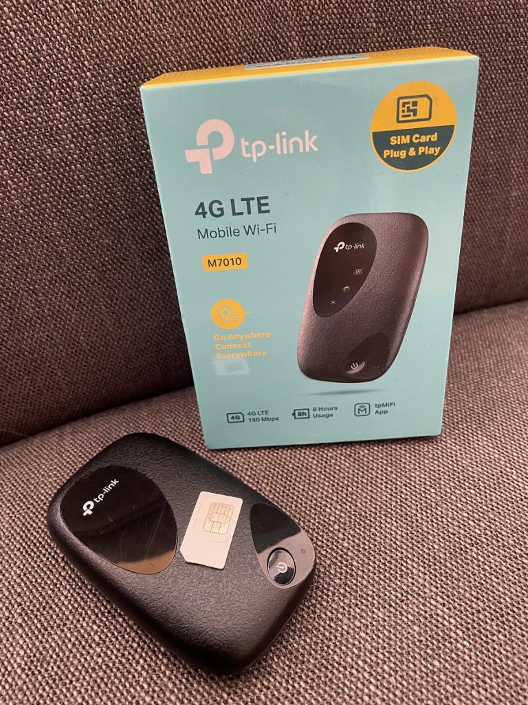 Der LTE Router TP-Link M7010 ausgepackt neben der Originalverpackung samt Sim-Karte für mobiles Internet im Auslandsurlaub.