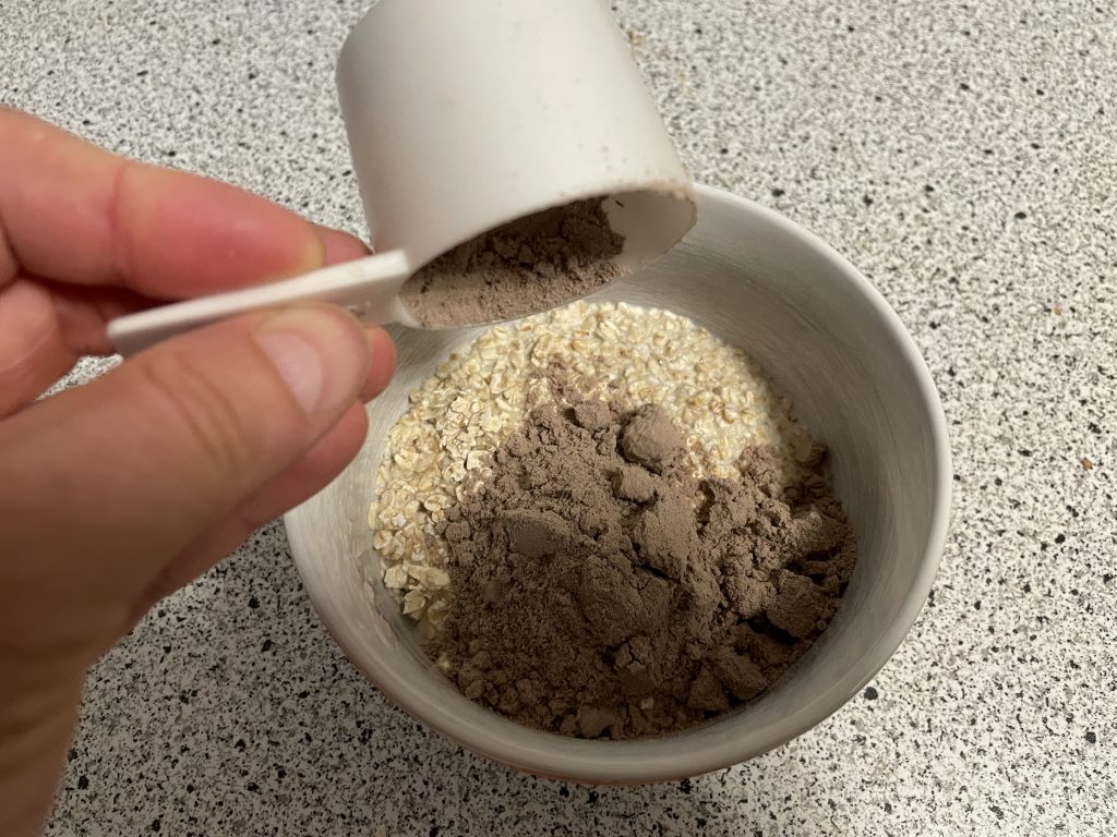 Essen und Ernährung - Mein gutes Beispiel für ein Frühstück: Tobi schüttet mit einem Dosierlöffel Proteinpulver Schokoladengeschmack in eine Schüssel mit Haferflocken und Milch.