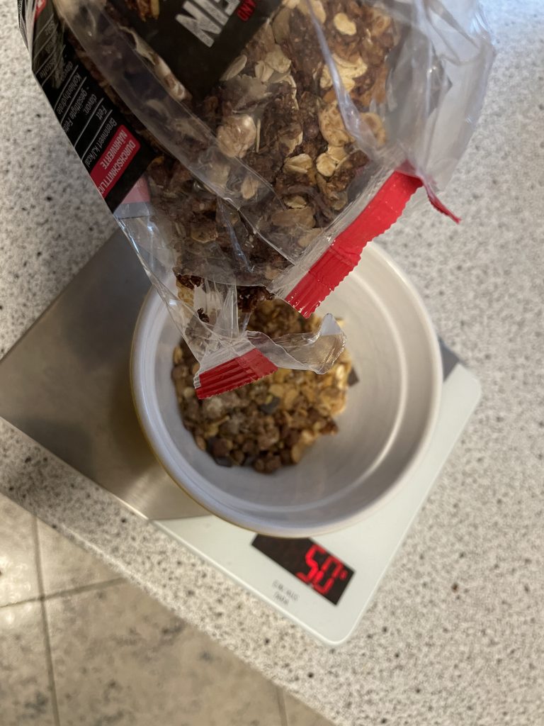 Essen und Ernährung - Mein gutes Beispiel für ein Frühstück: Tobi schüttet Proteinmüsli in eine Schüssel. Diese steht auf einer Küchenwaage und zeigt 50 g an.